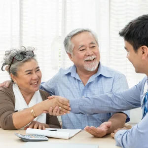 Older couple shaking hands with an advisor across a desk with paperwork