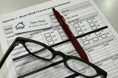 HECM financial analysis worksheet with reading glasses, a pen, and a name badge