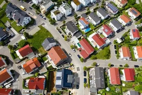 Aerial view of a suburban neighborhood with single-family homes, red and gray rooftops, and neatly arranged streets and green spaces.