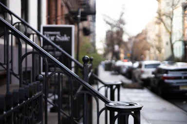 Wrought-iron stair railing beside a blurred city street with a for-sale sign