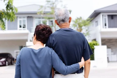 Couple viewed from behind with arms around each other facing a row of homes