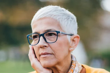 Older woman in a yellow cardigan resting her chin on her hand thoughtfully