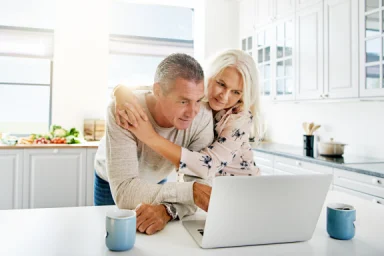 Couple in a kitchen looking together at a laptop with coffee mugs nearby