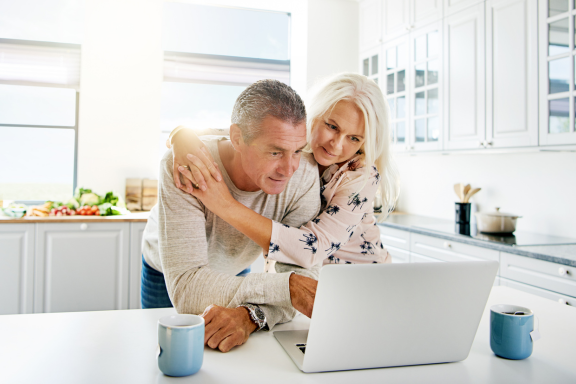 Couple in a kitchen looking together at a laptop with coffee mugs nearby