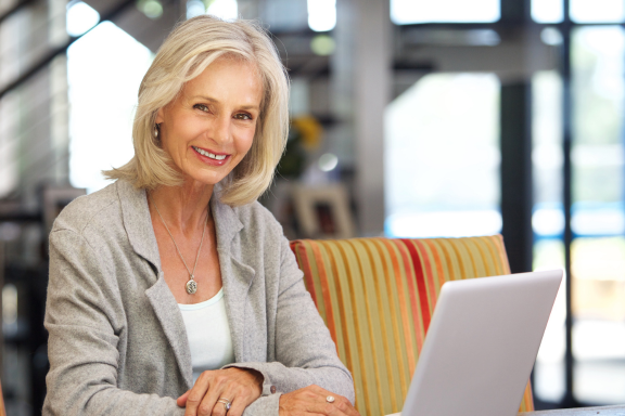 Smiling older woman sitting with a laptop in a bright indoor space