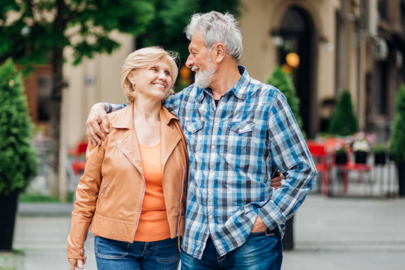Older couple smiling at each other while walking arm in arm outdoors