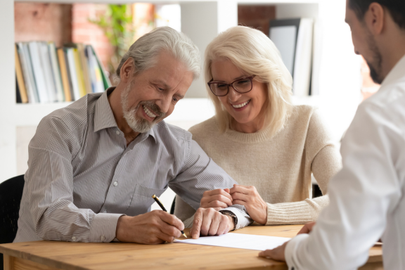 Older couple signing a document at a table across from an advisor