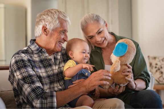 Grandparents and a baby playing with a stuffed animal on a couch