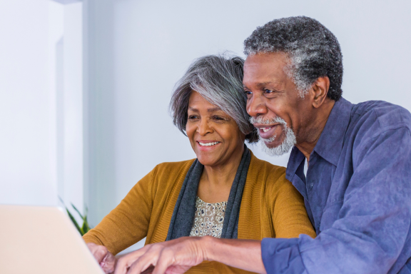 Older couple smiling together while looking at a laptop screen