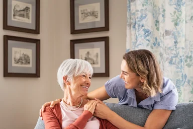Caregiver placing a comforting hand on an older woman's shoulder on a sofa