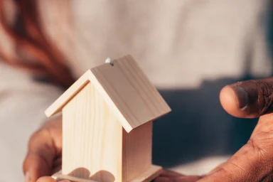 Two hands cupping a small wooden house model