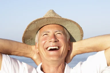 Man in a straw hat laughing with hands behind his head on a beach