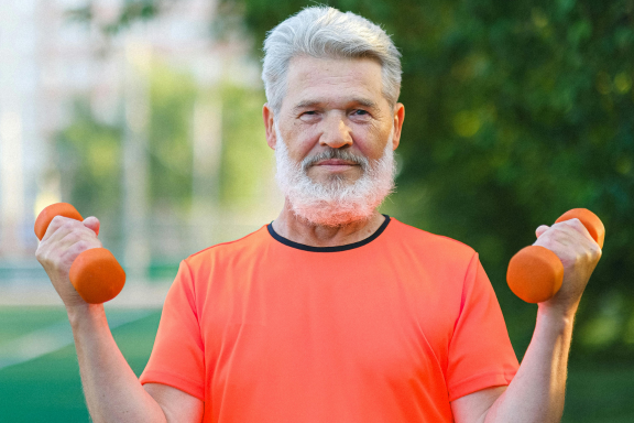 Older bearded man exercising outdoors with a pair of dumbbells