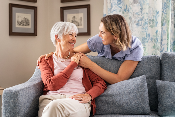 Caregiver placing a comforting hand on an older woman's shoulder on a couch