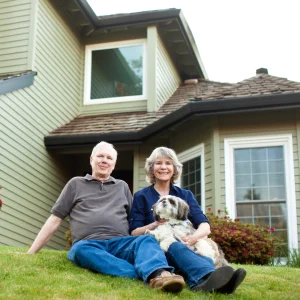 Couple sitting on the lawn with their dog in front of a two-story house