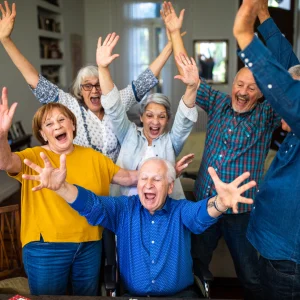 Group of older adults cheering with arms raised in a living room