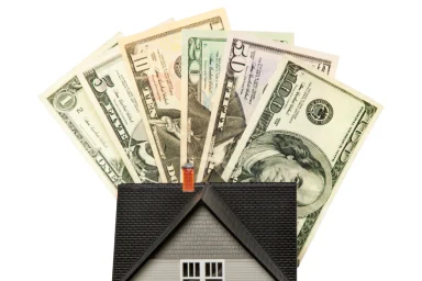 Fanned cash bills rising from the roof of a small model house