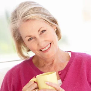 Smiling older woman in a pink cardigan holding a yellow coffee mug