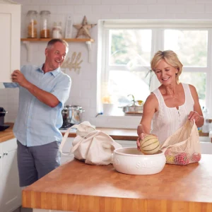 Couple in a kitchen unpacking a melon and vegetables from cloth grocery bags