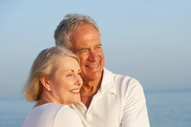 Older couple embracing on a beach at sunset, both smiling