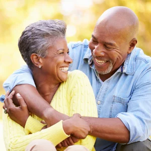 Laughing couple embracing outdoors, woman resting her head on his shoulder