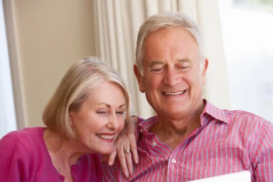 Older couple sitting together smiling while looking at a laptop screen