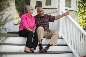 Older couple sitting on porch steps as the man points toward the distance
