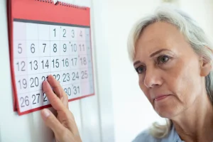 Older woman looking worried while marking a date on a wall calendar