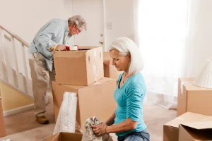 Older couple packing cardboard boxes near a staircase while moving
