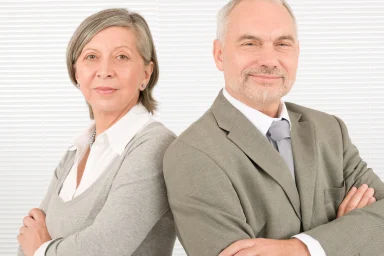 Older man and woman in business attire standing back to back, smiling