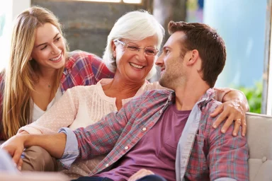 Older woman laughing on a couch between a younger woman and man