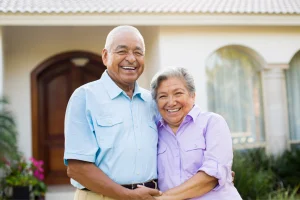 Smiling older couple standing arm in arm outside a stucco home entrance