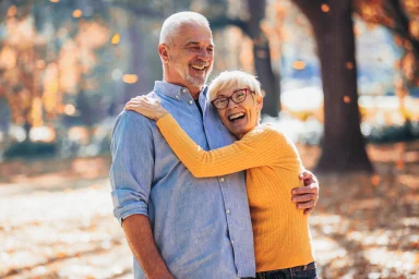 Older couple laughing and embracing outdoors among fall foliage