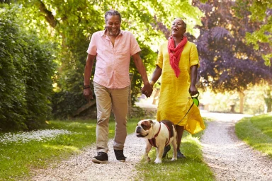 Older couple laughing and walking a bulldog together on a leash