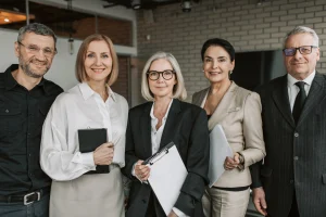 Five professionals in business attire standing together holding folders and tablets