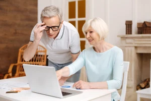 Older man looking concerned while his wife points at a laptop screen