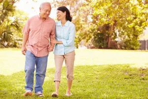 Older couple holding hands and smiling while walking across a grassy lawn