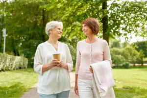 Two women chatting and walking together along a tree-lined park path