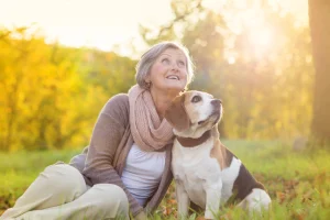 Smiling older woman sitting outdoors with her beagle in autumn light