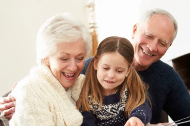 Grandparents reading a picture book with their granddaughter on a couch