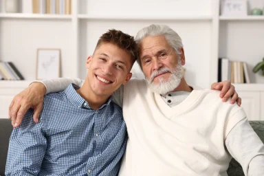 Young man and older man with arms around each other on a sofa