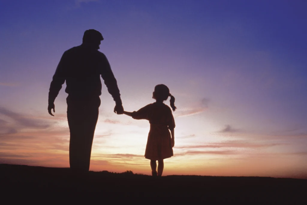 Silhouette of a father and young daughter holding hands at sunset