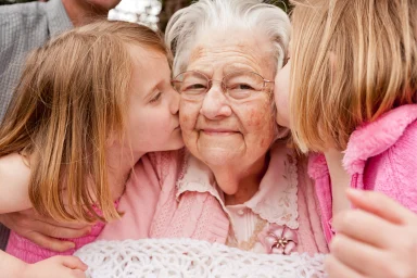 Two young girls kissing their smiling grandmother on the cheek outdoors