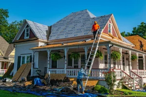 Roofing crew laying new shingles on a Victorian house's steep roofline