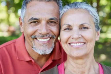 Older man and woman smiling cheek to cheek outdoors among green trees