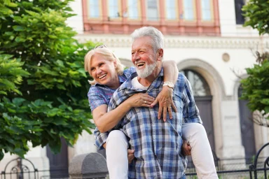 Laughing man giving a woman a piggyback ride in front of a historic building
