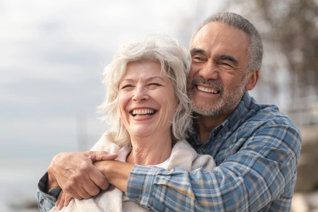 Older couple embracing and laughing outdoors near the water
