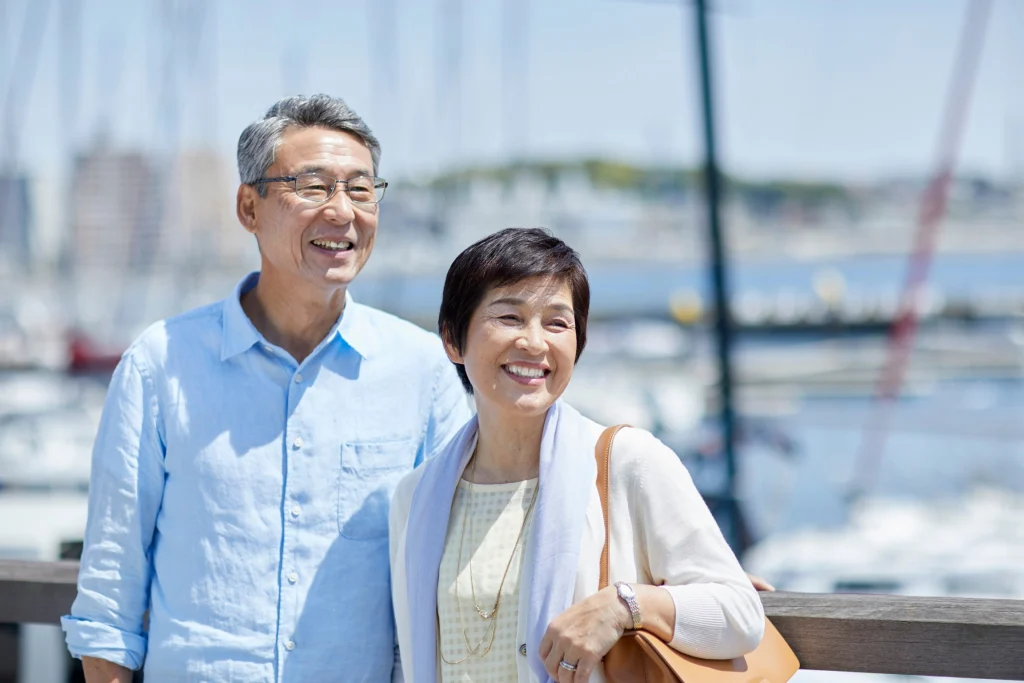 Older couple smiling together at a marina with sailboats behind them