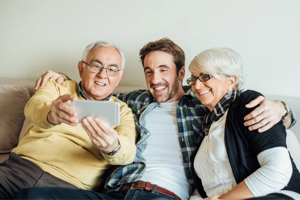 Older couple and their adult son smiling for a selfie on a couch