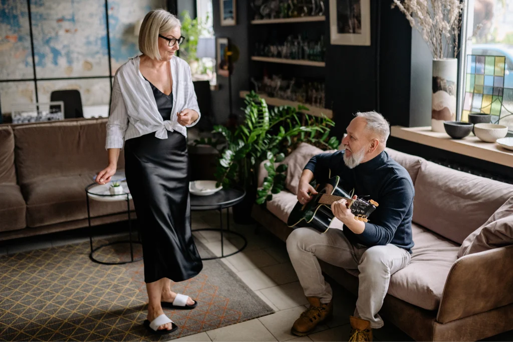 Woman dancing while a man plays acoustic guitar on the couch beside her